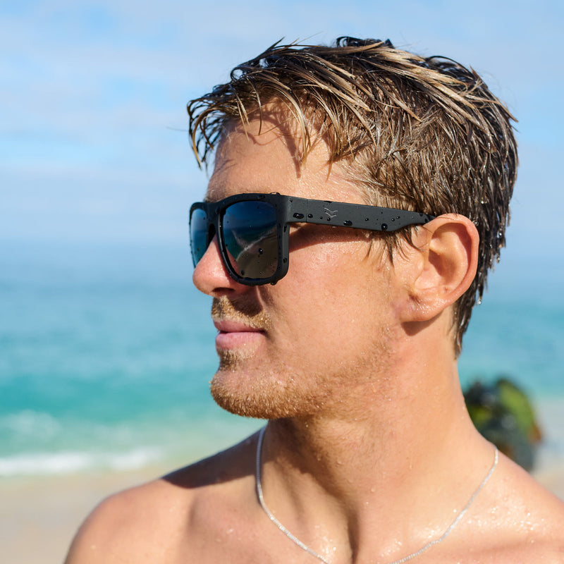 Man wearing sunglasses on a beach with ocean and sky in the background