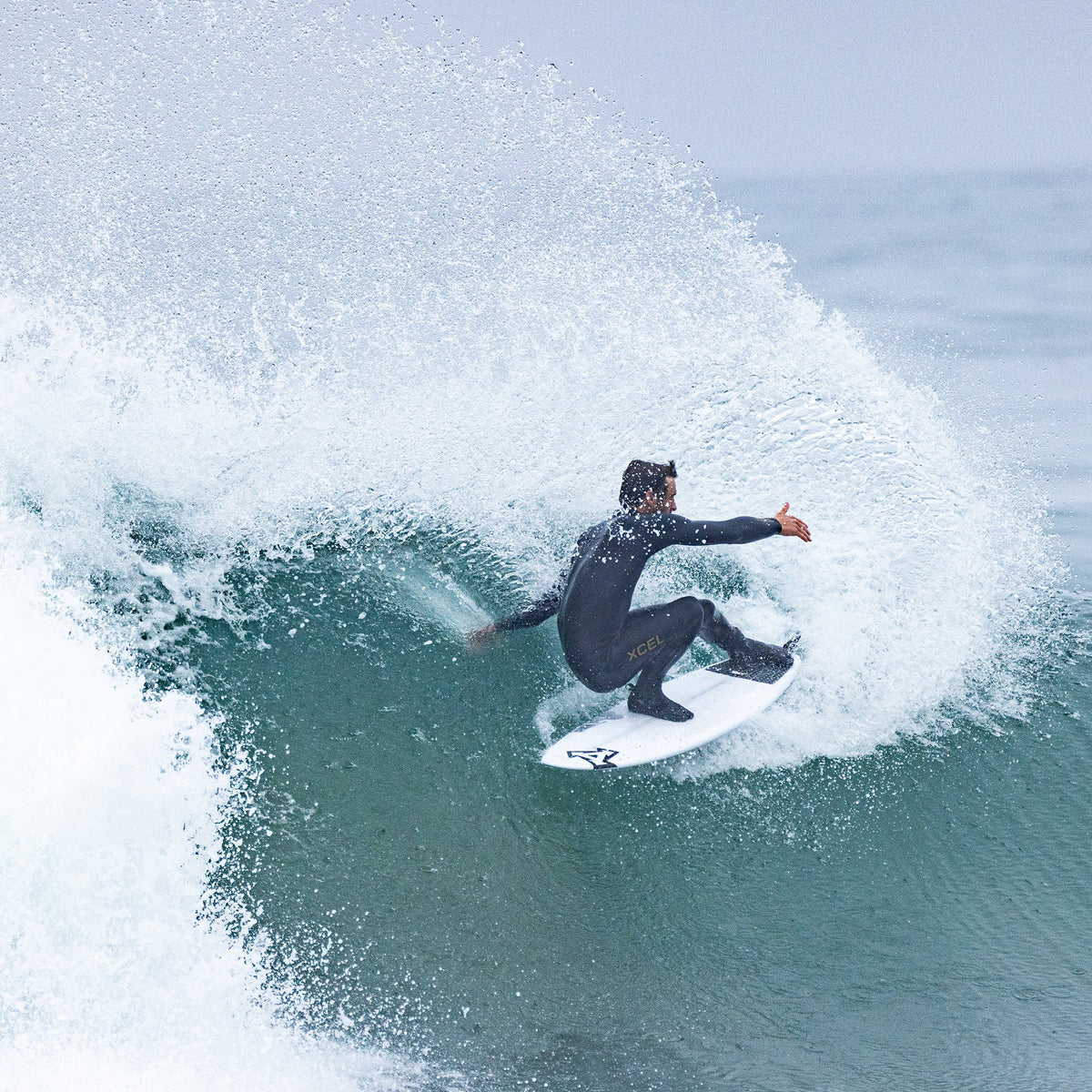Surfer in a wetsuit riding a wave with a large splash.