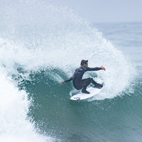 Surfer in a wetsuit riding a wave with a large splash.