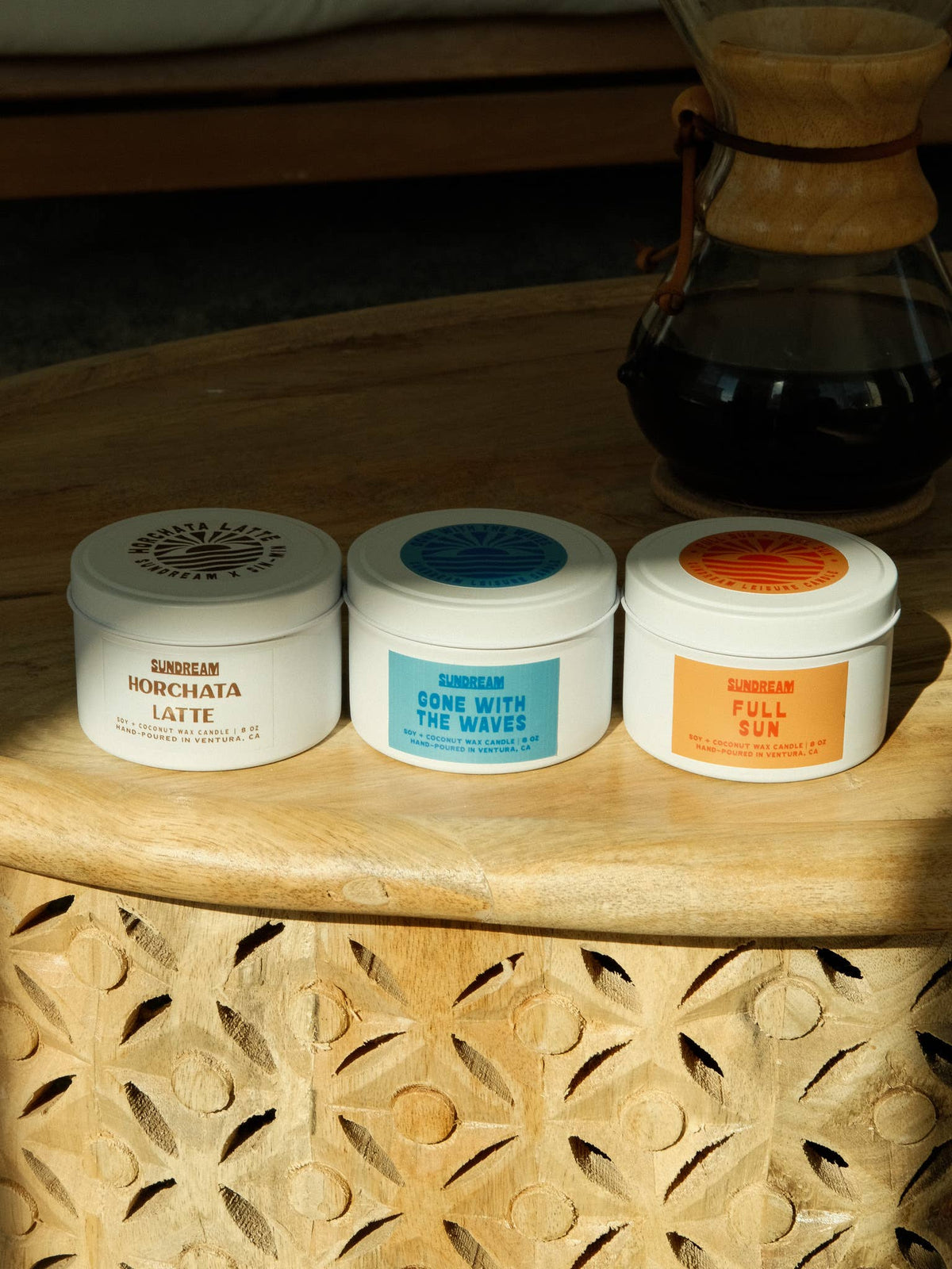 Three containers of Sundream products on a wooden surface with a coffee maker in the background.