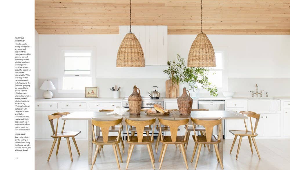 Modern kitchen with wooden dining table and chairs, white cabinets, and pendant lights.