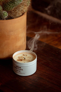 Candle labeled 'Espresso Mocchiatto' with a smoking wick next to a potted cactus on a wooden surface.