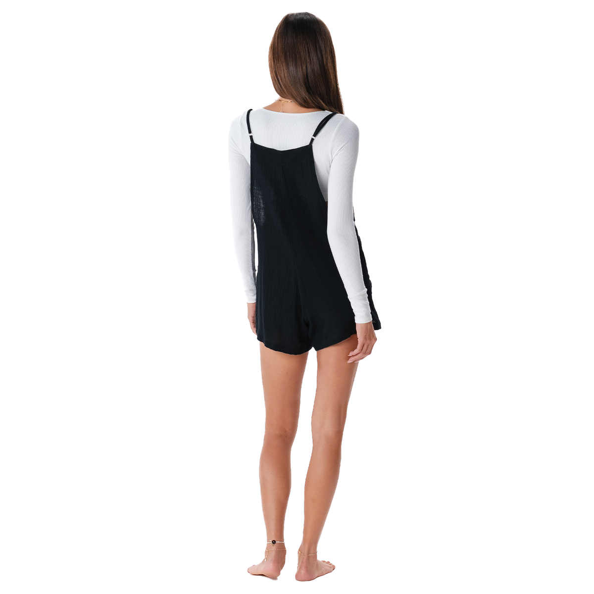 Person wearing a black pinafore over a white long-sleeve shirt on a white background