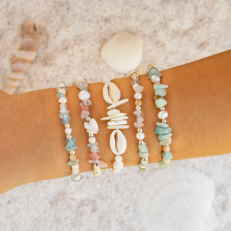 Beach-themed bracelet set on a wrist with a sand background