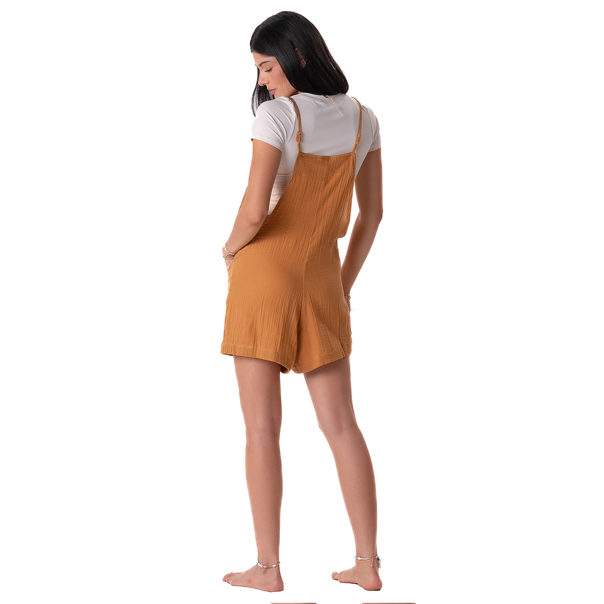 Woman wearing a mustard yellow pinafore dress over a white shirt on a white background