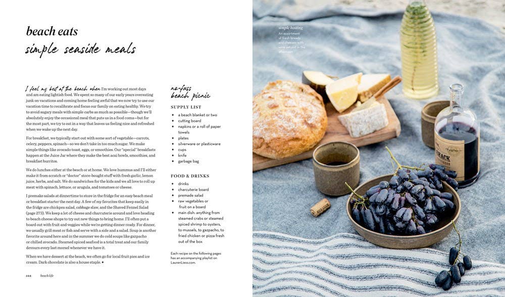 Seaside meal setup with bread, cheese, and wine on a striped fabric.