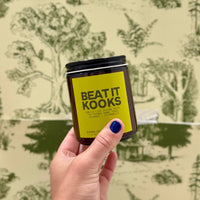 Hand holding a jar labeled 'Beat It Kooks' against a patterned background