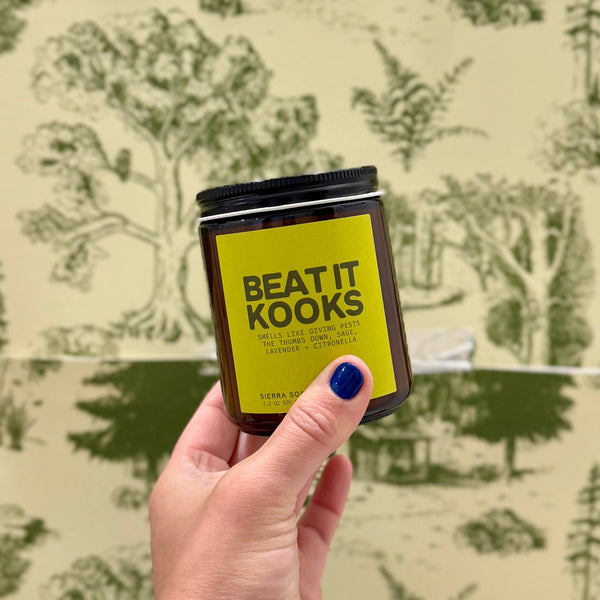 Hand holding a jar labeled 'Beat It Kooks' against a patterned background
