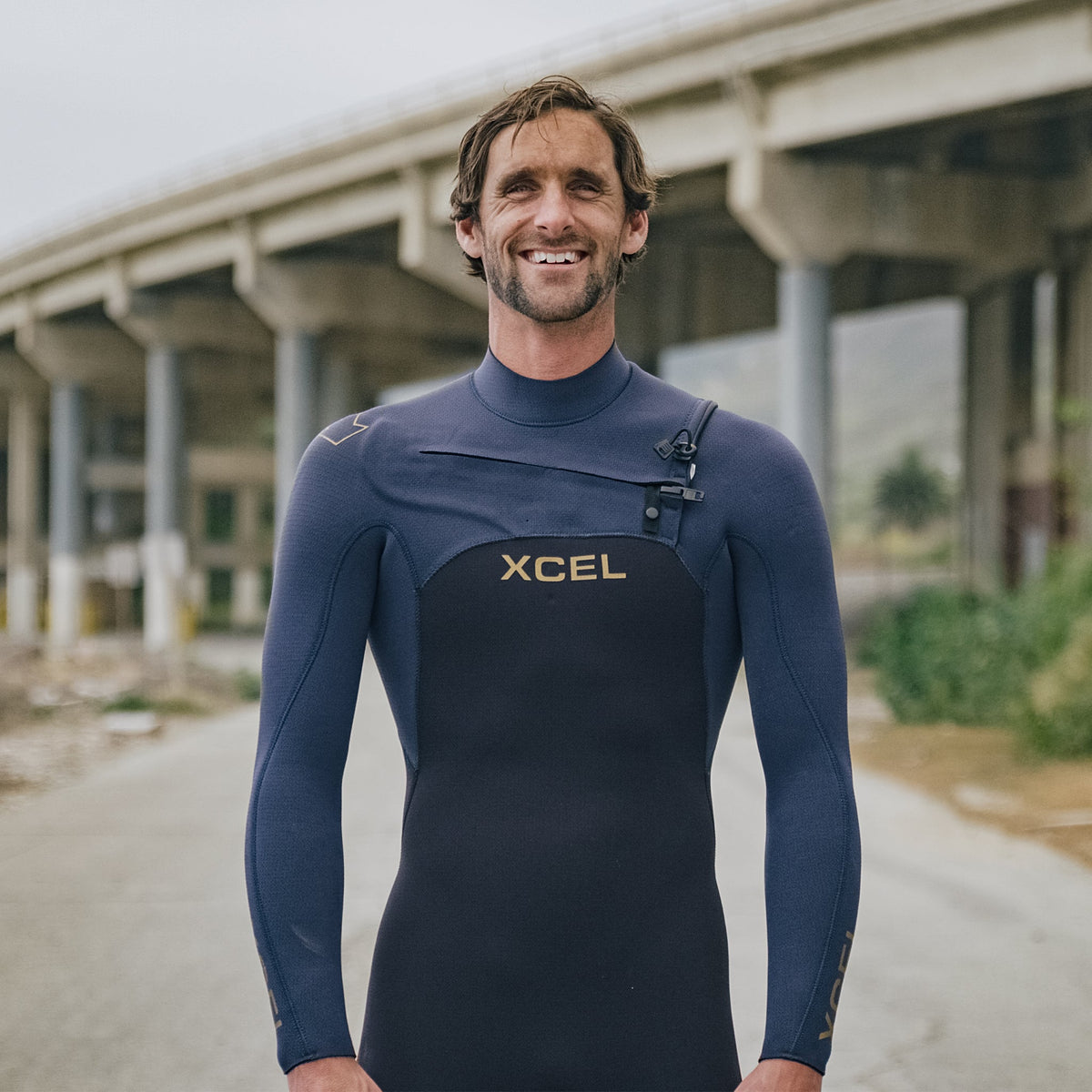 Man wearing a blue XCEL wetsuit standing outdoors with a blurred background