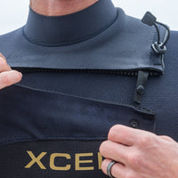Person wearing a navy blue wetsuit with 'XCEL' branding, focusing on the chest area.