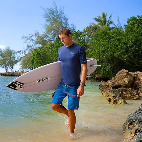 Man holding a surfboard on a beach with trees and clear sky in the background