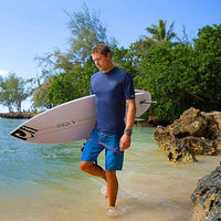 Man holding a surfboard on a beach with trees and clear sky in the background