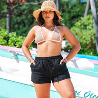 Woman in a bikini and sun hat by a poolside with greenery in the background