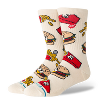 A pair of crew socks in a warm off-white/cream color, featuring a colorful cartoon pattern of burgers, french fries, and red Stutz logos.