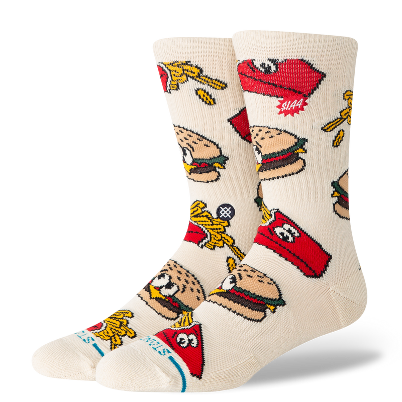 A pair of crew socks in a warm off-white/cream color, featuring a colorful cartoon pattern of burgers, french fries, and red Stutz logos.