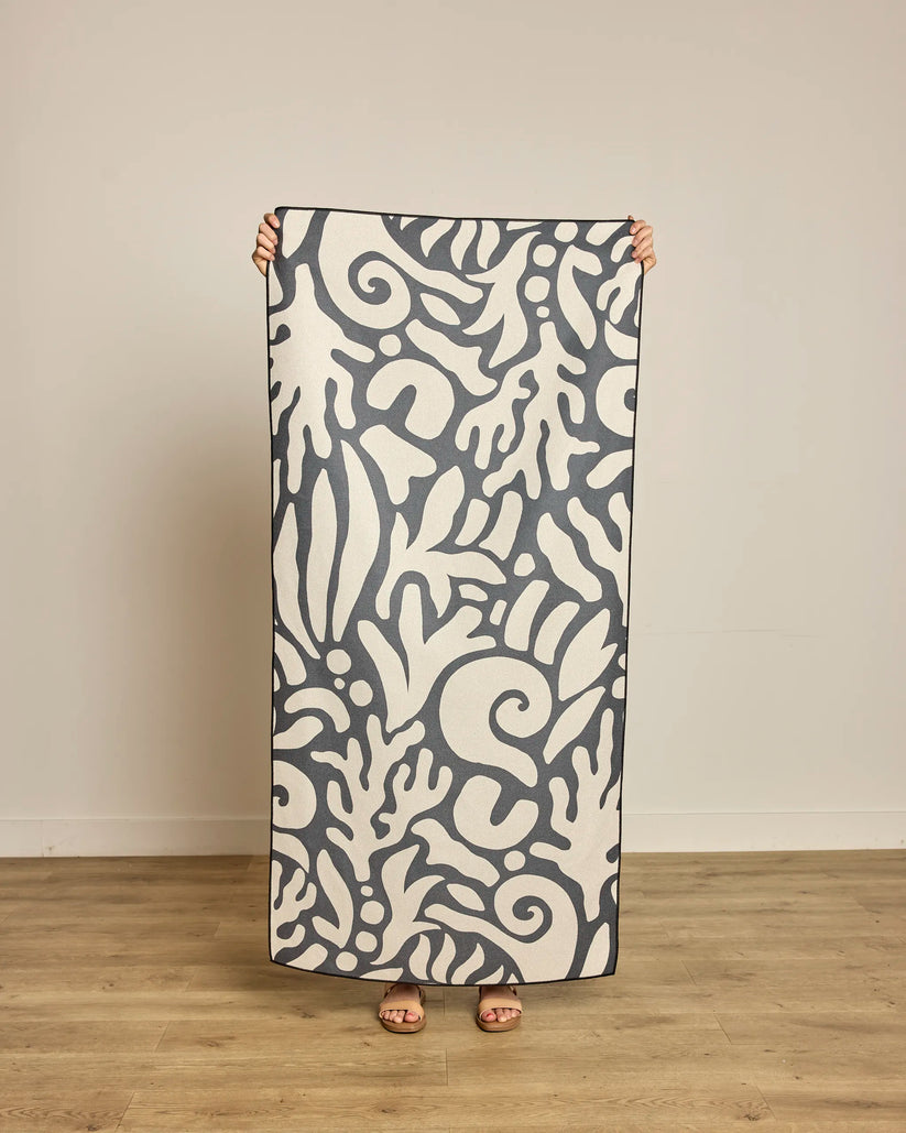 Person holding a large towel with a white pattern on a wooden floor.