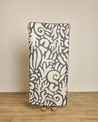Person holding a large towel with a white pattern on a wooden floor.