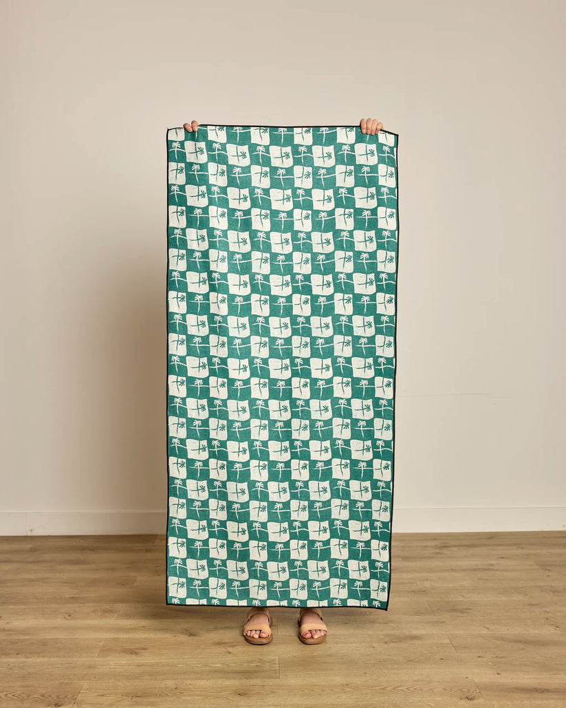 Person holding a green and white patterned towel on a wooden floor.