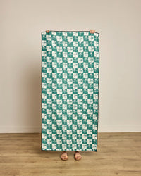 Person holding a green and white patterned towel on a wooden floor.