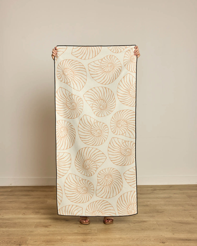 Person holding a decorative blanket with shell pattern on a wooden floor.
