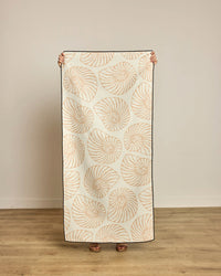 Person holding a decorative blanket with shell pattern on a wooden floor.
