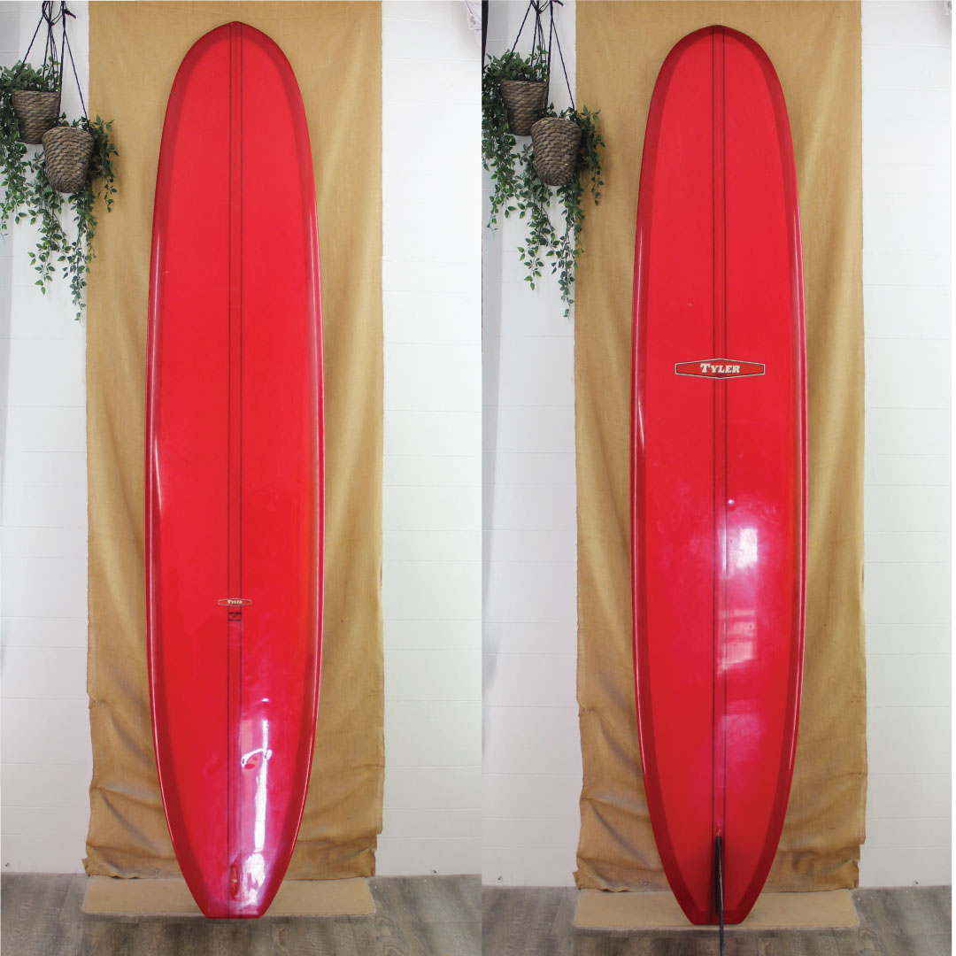 Two red surfboards standing side by side against a beige curtain with plants hanging above.
