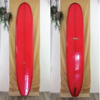 Two red surfboards standing side by side against a beige curtain with plants hanging above.