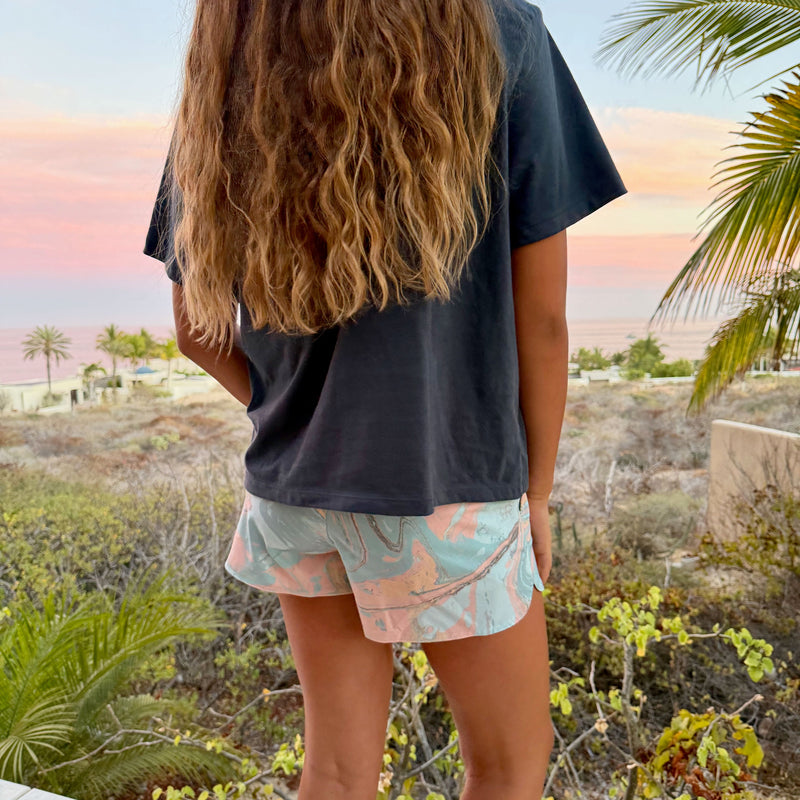 Person wearing a dark t-shirt and patterned shorts standing with their back to the camera, overlooking a scenic landscape.