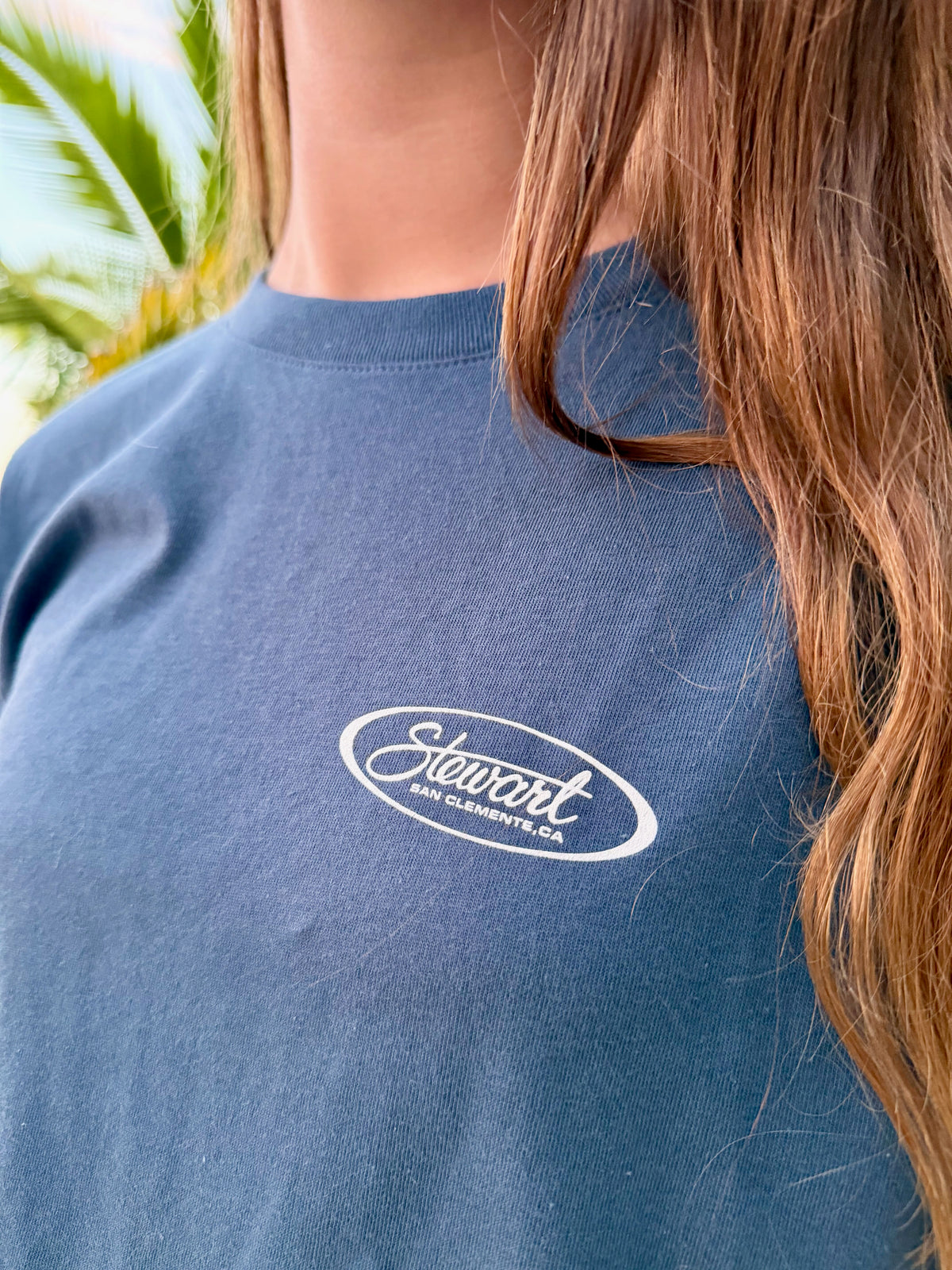 Person wearing a blue shirt with 'Stewart' logo, palm trees in the background