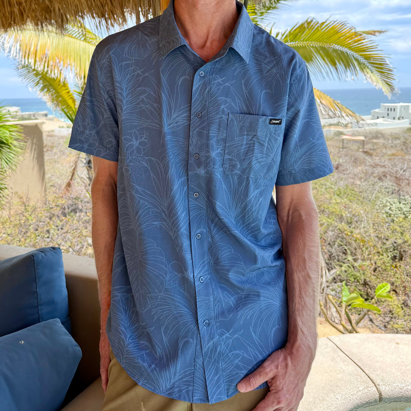 man wearing a blue button-up shirt with palm trees and ocean in the background