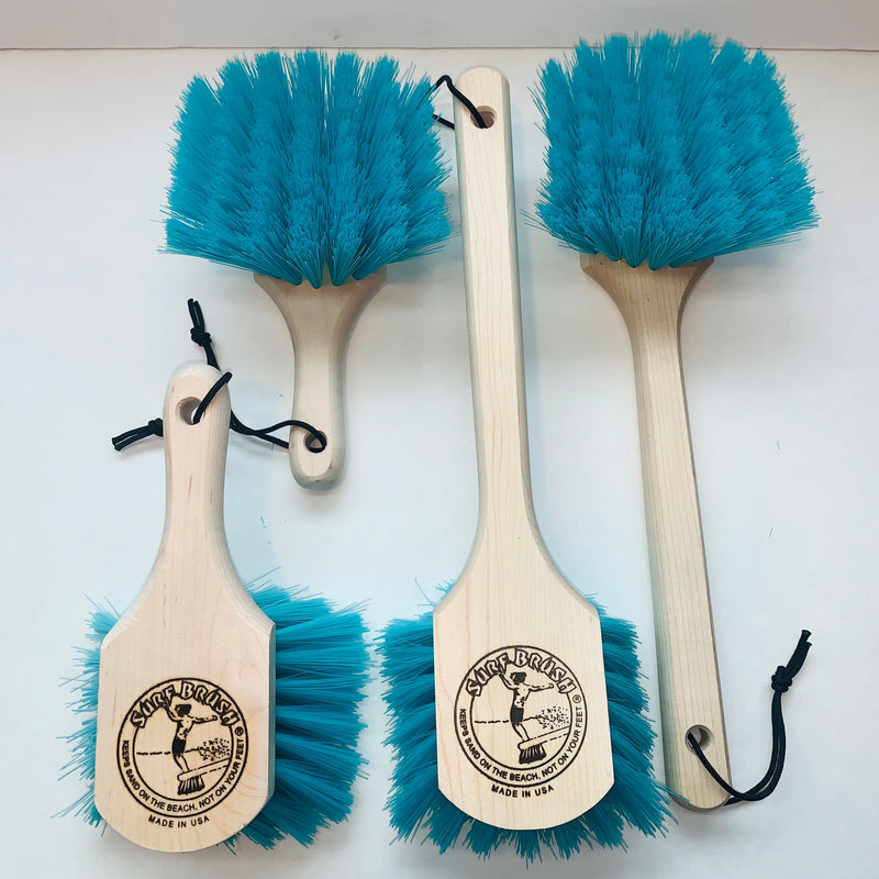 A surf brush with a long wooden handle and green bristles, featuring a logo on the handle.