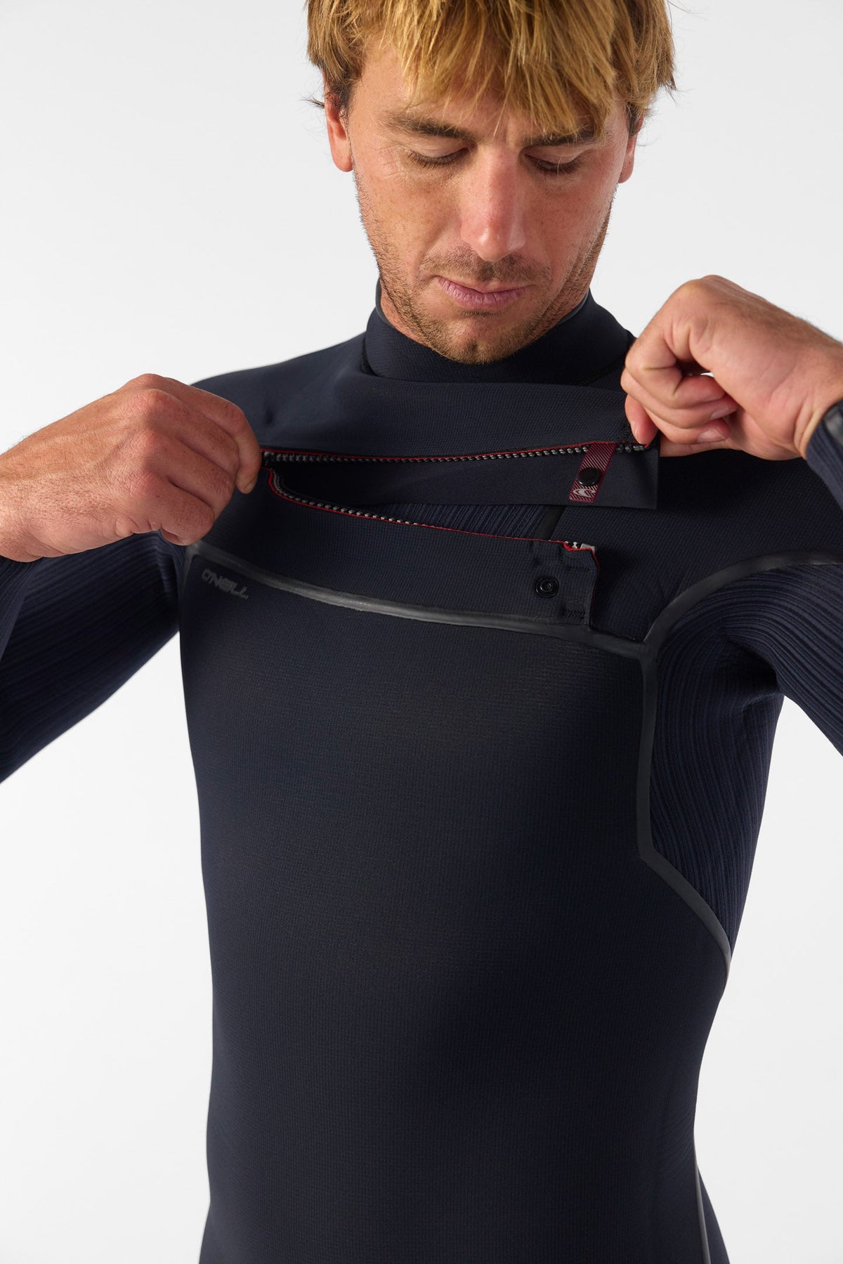 Person wearing a black wetsuit adjusting the chest zipper against a white background
