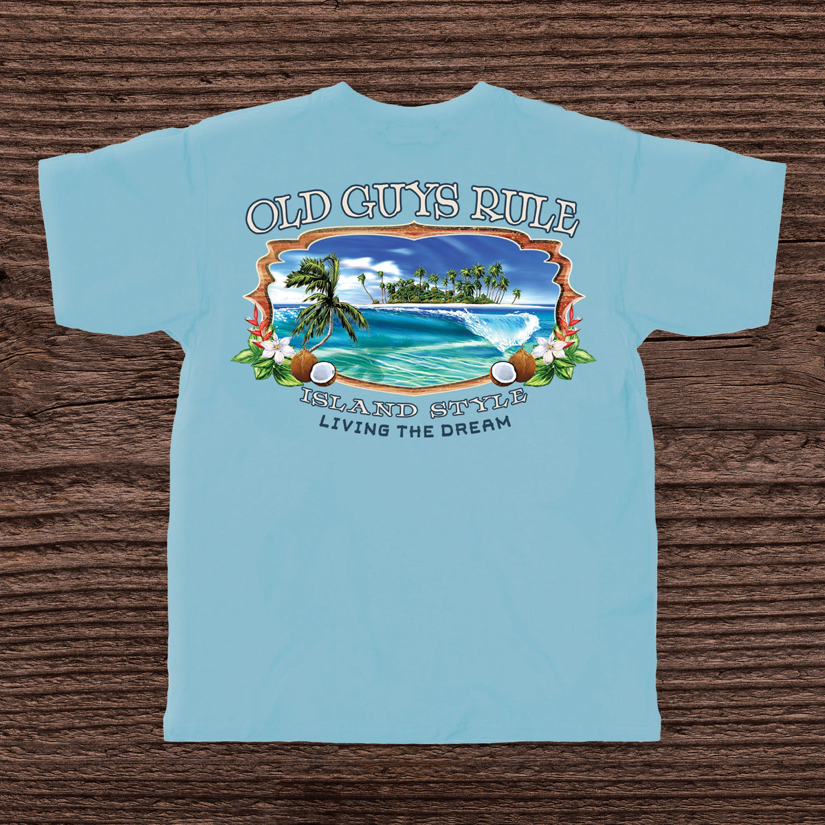 Light blue t-shirt with tropical island graphic and 'Old Guys Rule' text on a wooden surface