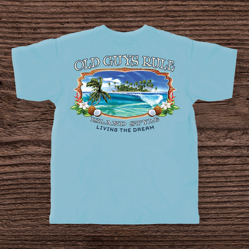 Light blue t-shirt with tropical island graphic and 'Old Guys Rule' text on a wooden surface