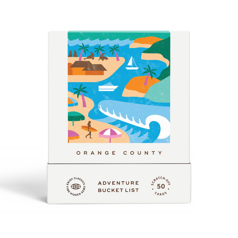 A boxed card product labeled 'ORANGE COUNTY' and 'ADVENTURE BUCKET LIST' with '50 scratch-off cards' on the front. The box is white with a colorful illustrated tropical coastal scene on the upper panel.
