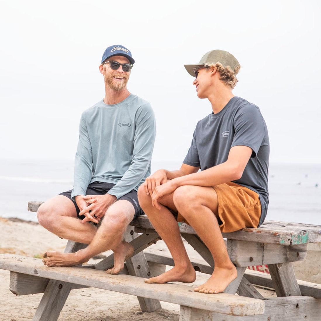 two guys sitting on a picnic table at the beach