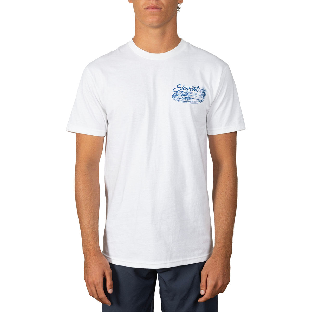 A man wearing a white crewneck t-shirt with a blue 'stewart' graphic on the left chest, paired with dark navy pants, against a plain white background.