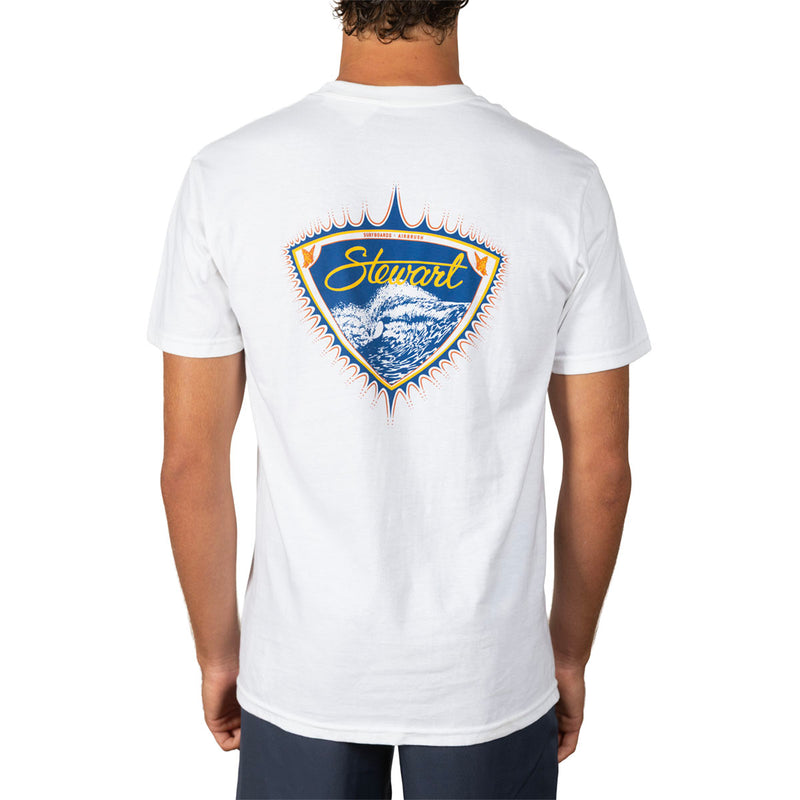 A man viewed from the back wearing a white short-sleeve t-shirt with a large graphic on the back. The graphic is a shield shape featuring blue ocean waves, a yellow surfboard, and the word 'Stewart' in yellow script.