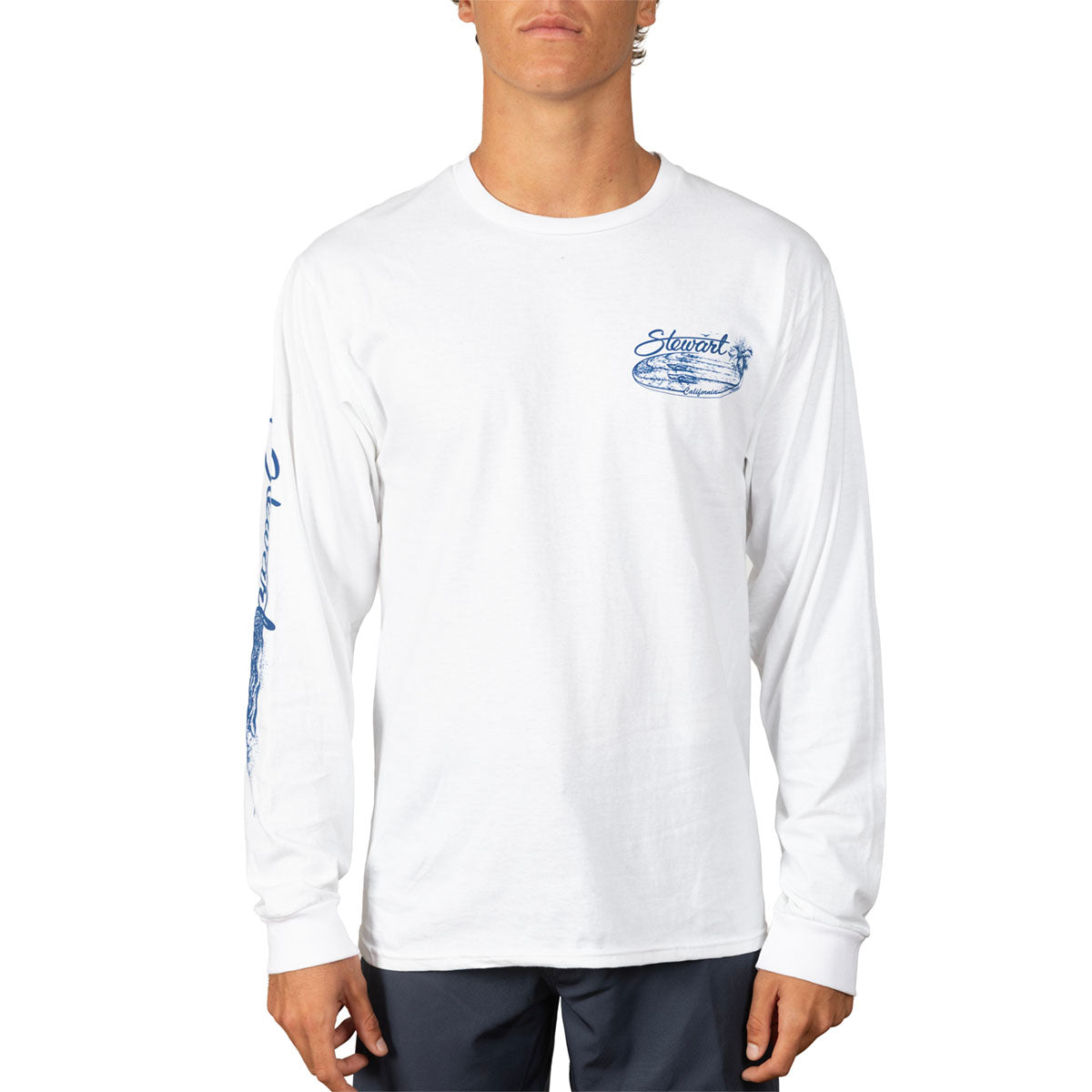 A man wearing a white long-sleeve t-shirt with blue graphic prints on the chest and sleeve, paired with dark pants, against a plain white background.