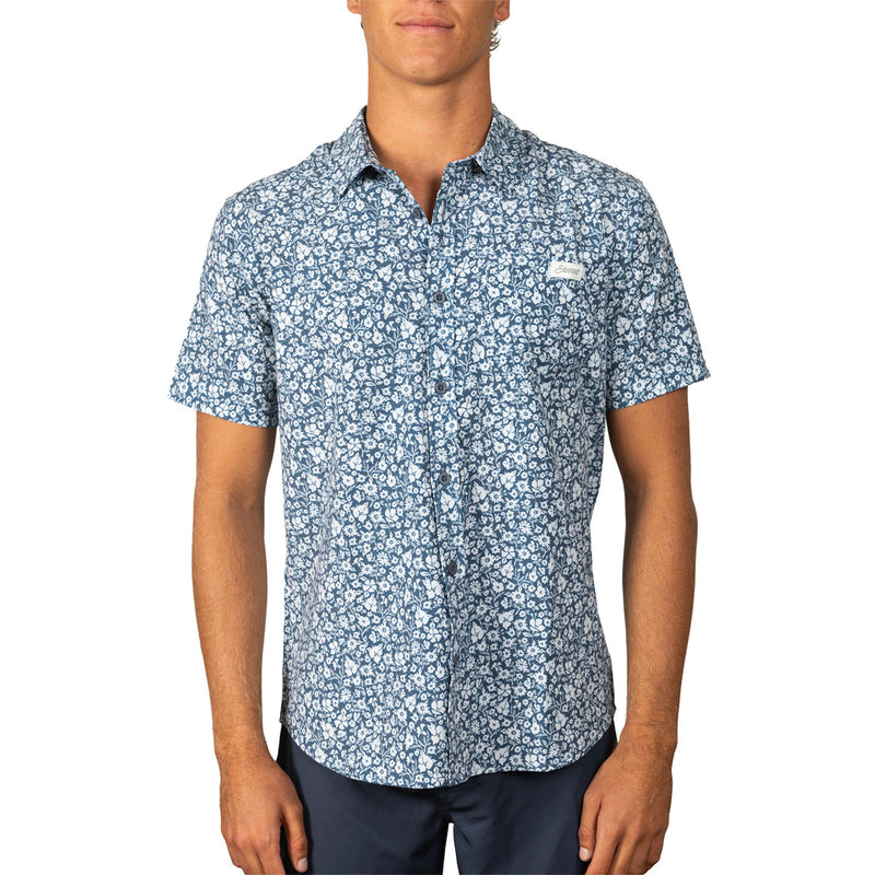 A man wearing a short-sleeve button-up shirt with a blue and white floral pattern, shown from the waist up against a plain white background.