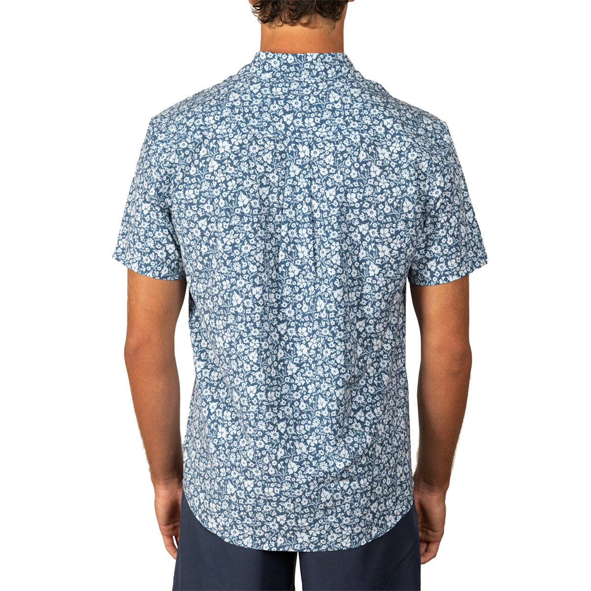 A man viewed from the back wearing a short-sleeve button-up shirt with a dense blue and white floral pattern, paired with dark navy pants, against a plain white background.