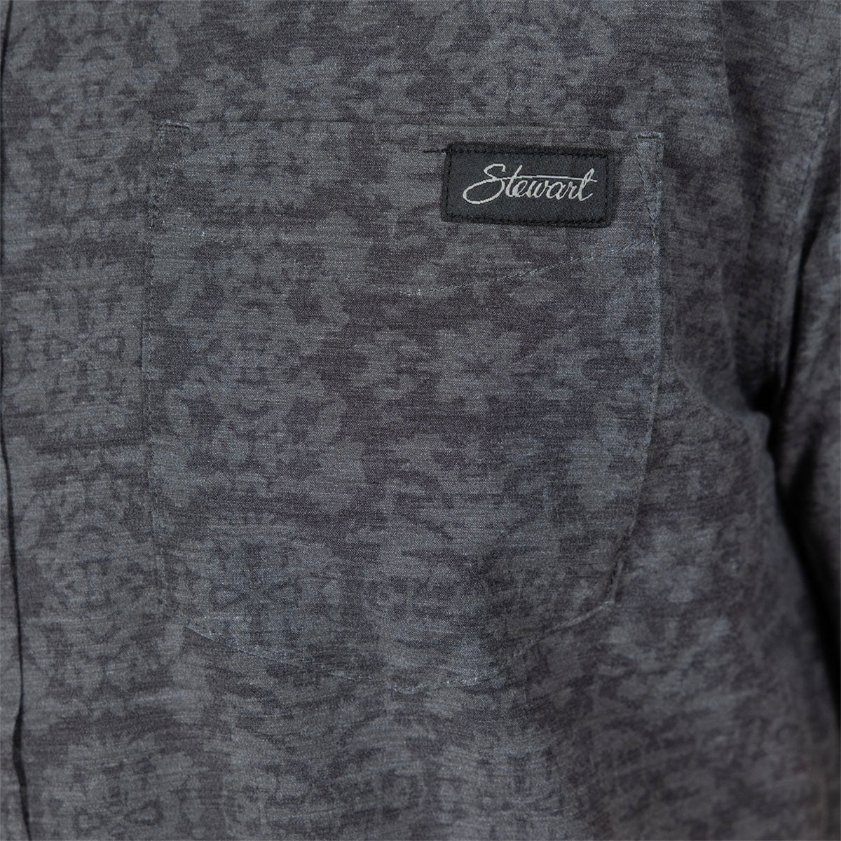 Close-up of a dark gray textured fabric garment with a chest pocket and a black embroidered 'Stewart' brand patch.