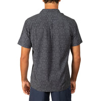 A man viewed from the back wearing a dark gray short-sleeve button-up shirt with a subtle geometric pattern, paired with navy pants, against a plain white background.