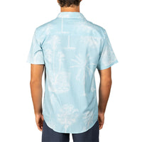 A man viewed from the back wearing a light blue short-sleeve button-up shirt with a white tropical palm tree and beach print, paired with dark blue pants, against a plain white background.