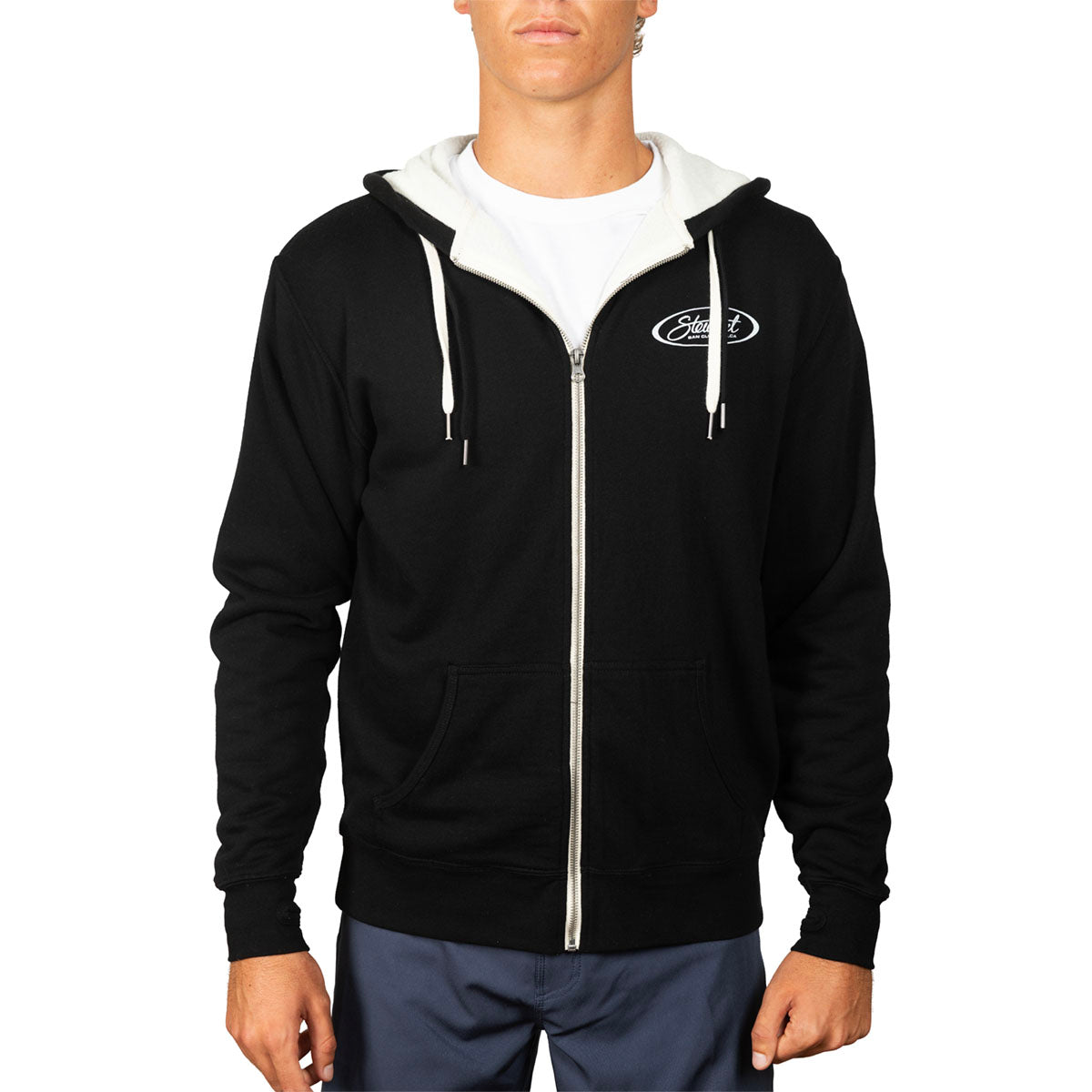 A man wearing a black zip-up hoodie with a white hood lining, white drawstrings, and a white vertical zipper. The hoodie features a white oval chest logo that reads 'Ford'.
