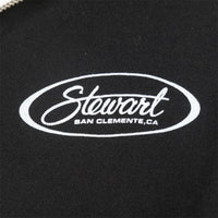 Close-up of a black fabric surface with a white embroidered oval logo reading 'Stewart' and smaller text 'SAN CLEMENTE,CA'.