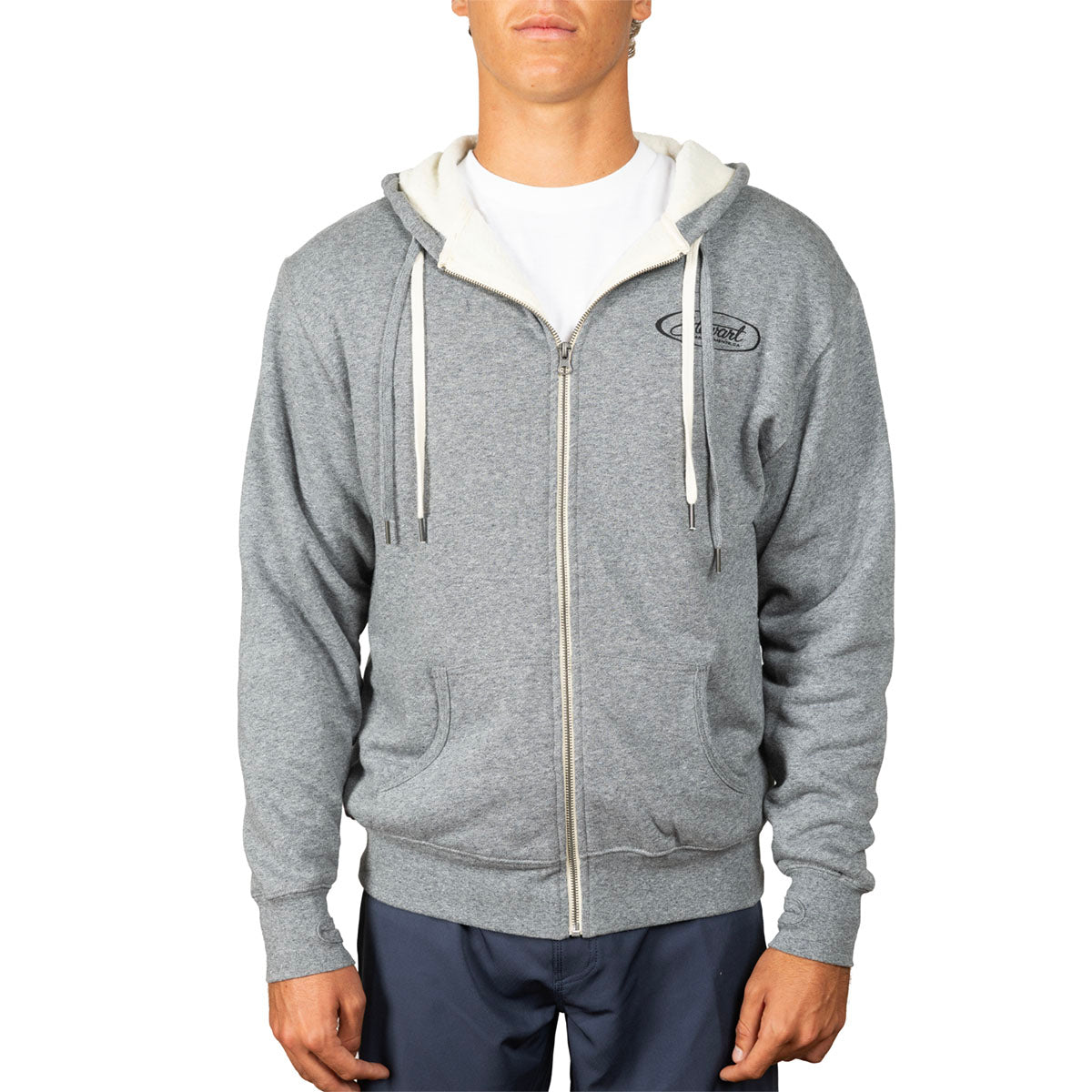 A man wearing a heather gray zip-up hoodie with a cream-colored hood lining and white drawstrings, layered over a white t-shirt and navy blue pants, against a plain white background.