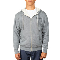 A man wearing a heather gray zip-up hoodie with a cream-colored hood lining and white drawstrings, layered over a white t-shirt and navy blue pants, against a plain white background.