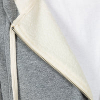 Close-up detail of a gray zippered hoodie with a cream-colored fleece lining and matching drawstring, shown against a white background.