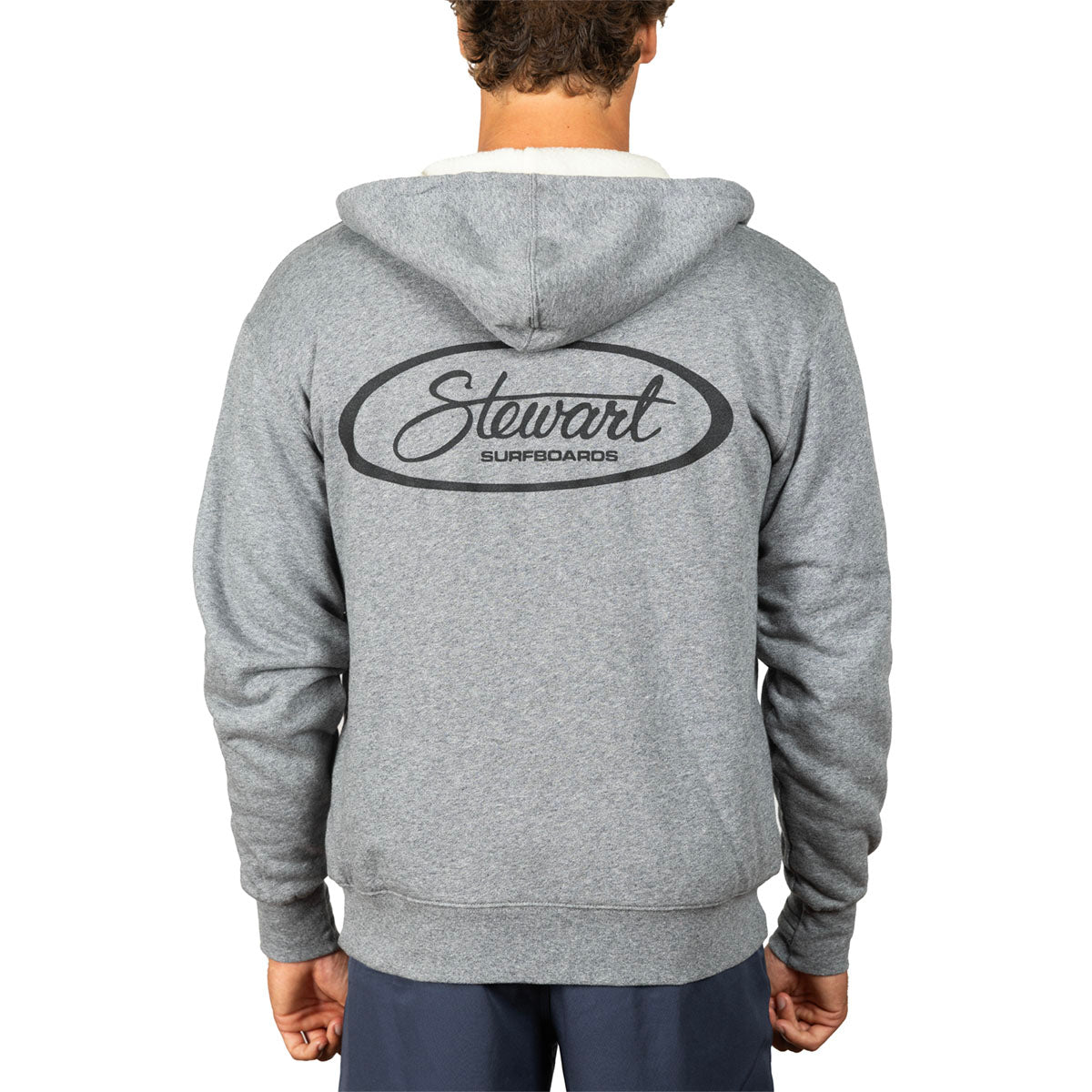 A person shown from the back wearing a heather gray hooded sweatshirt with a large black oval 'Stewart Surfboards' logo printed across the upper back, against a plain white studio background.